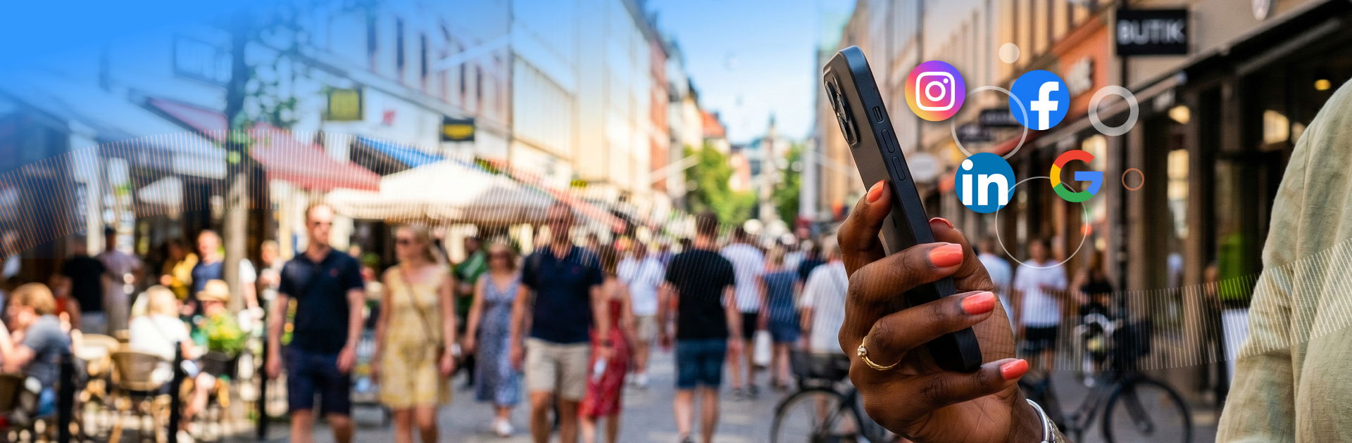 Hand holding a phone on a busy shopping street, surrounded by social media platform icons